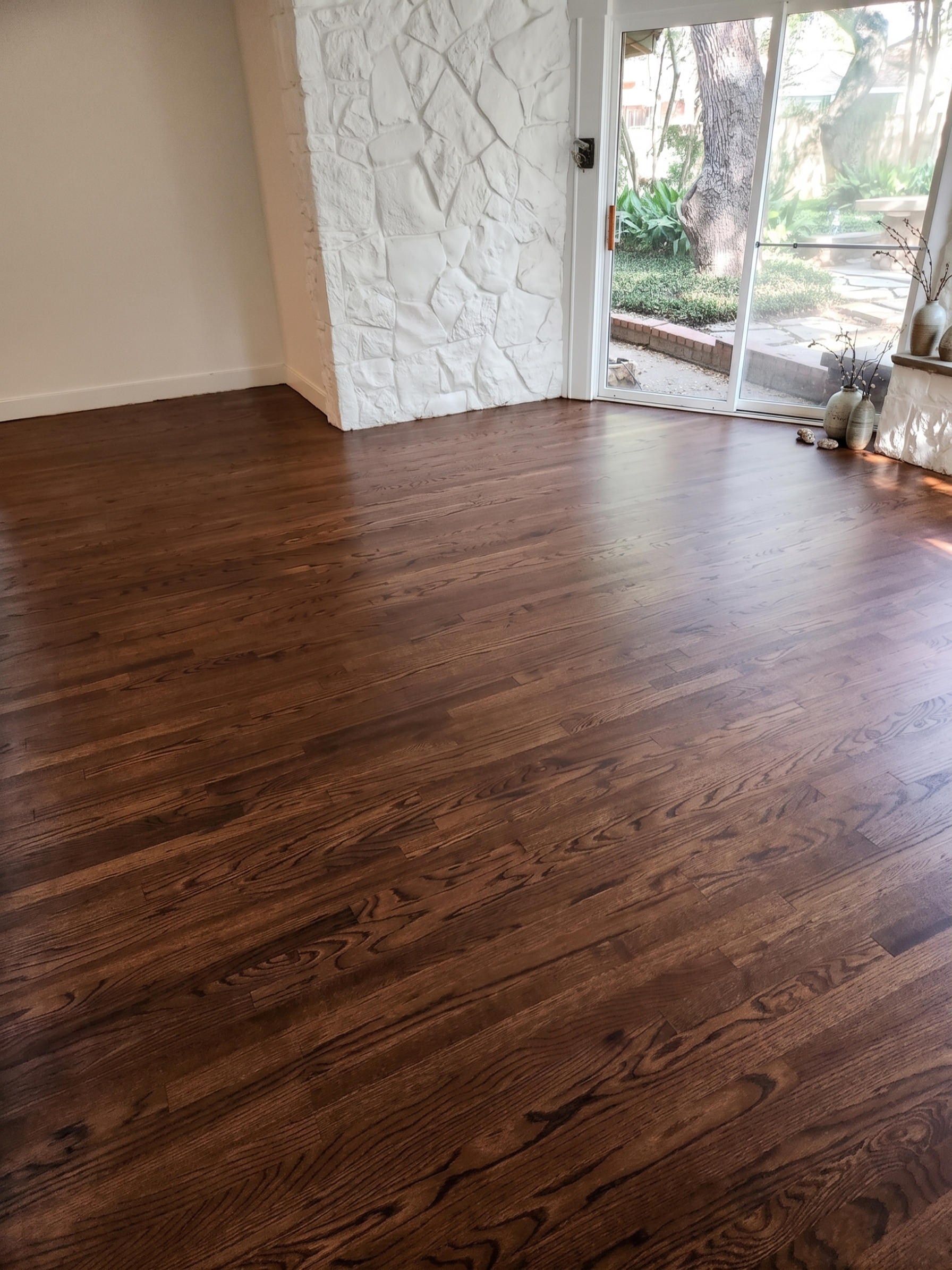 Empty room with dark wood flooring, stone fireplace wall, and sliding glass doors to a patio.