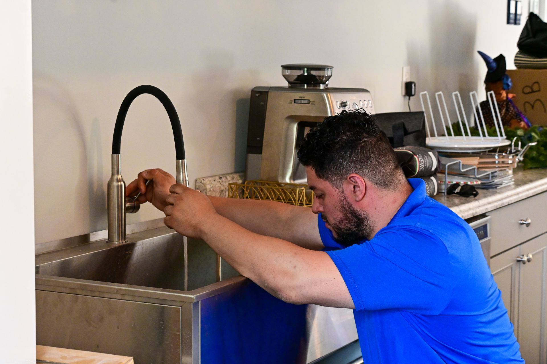A man in a blue shirt is fixing a faucet in a kitchen.