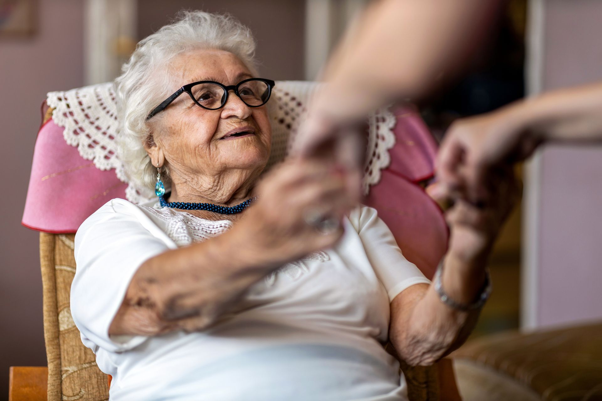 An elderly woman is sitting in a chair holding a person 's hand.
