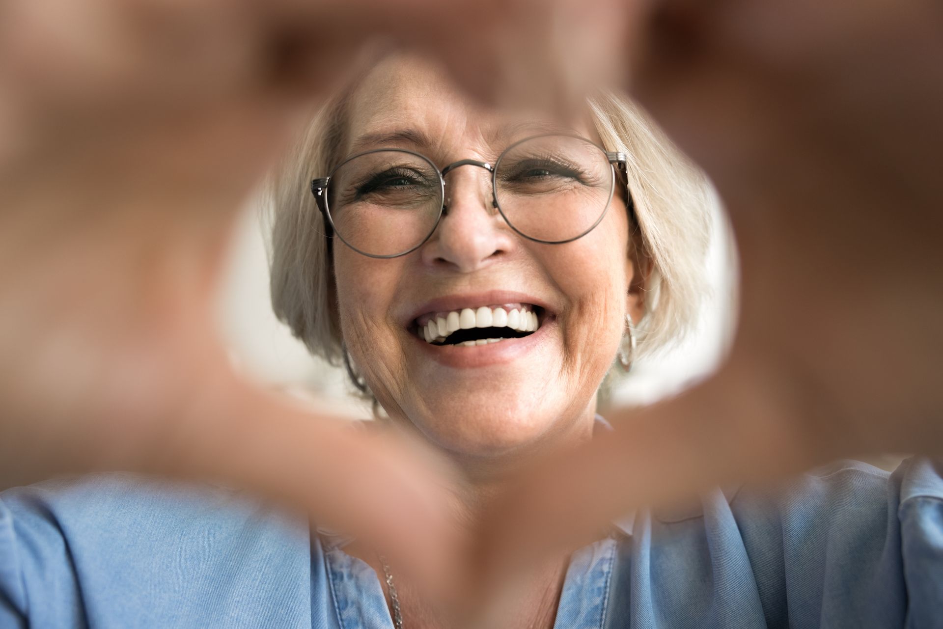 A woman wearing glasses is making a heart shape with her hands.