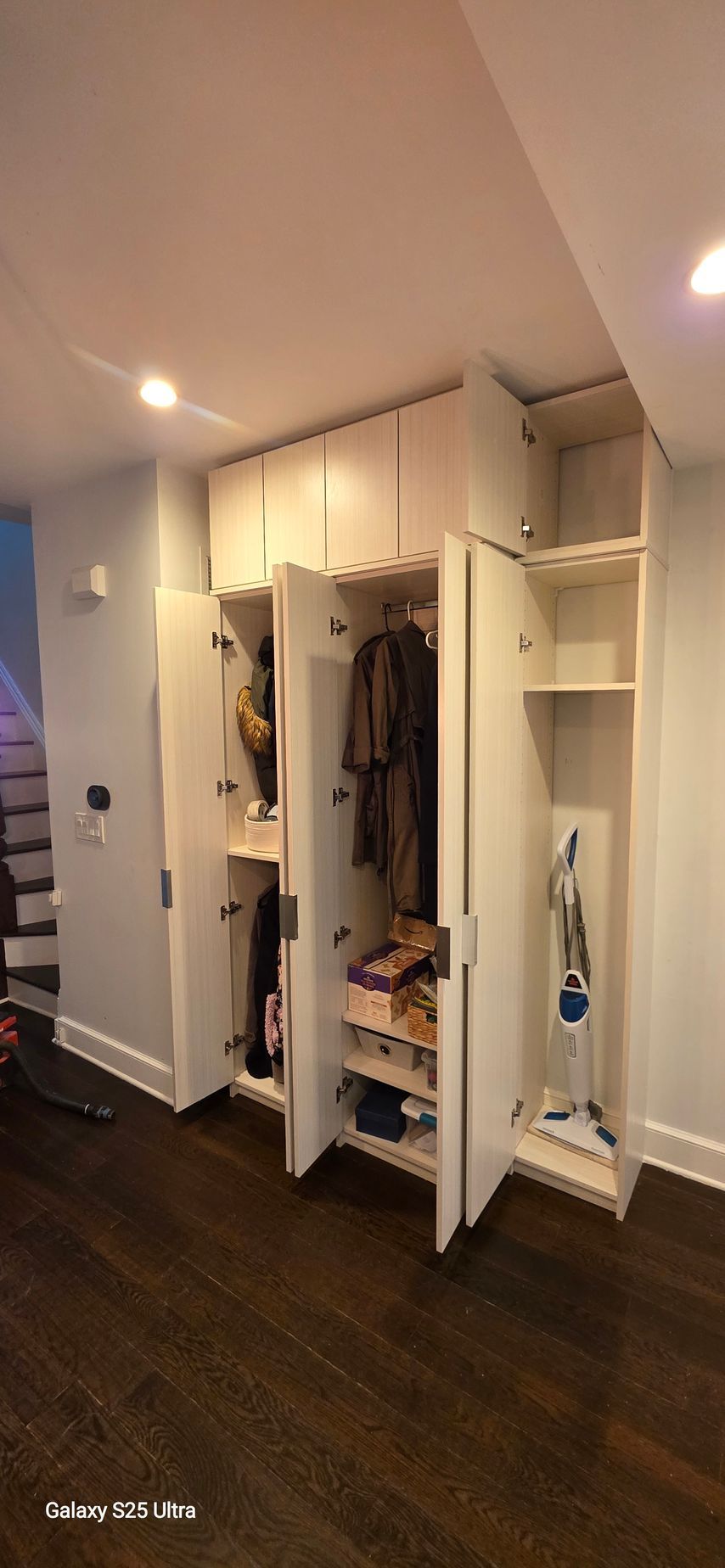 A built-in closet with open doors reveals storage for clothes, shoes, and a vacuum cleaner.