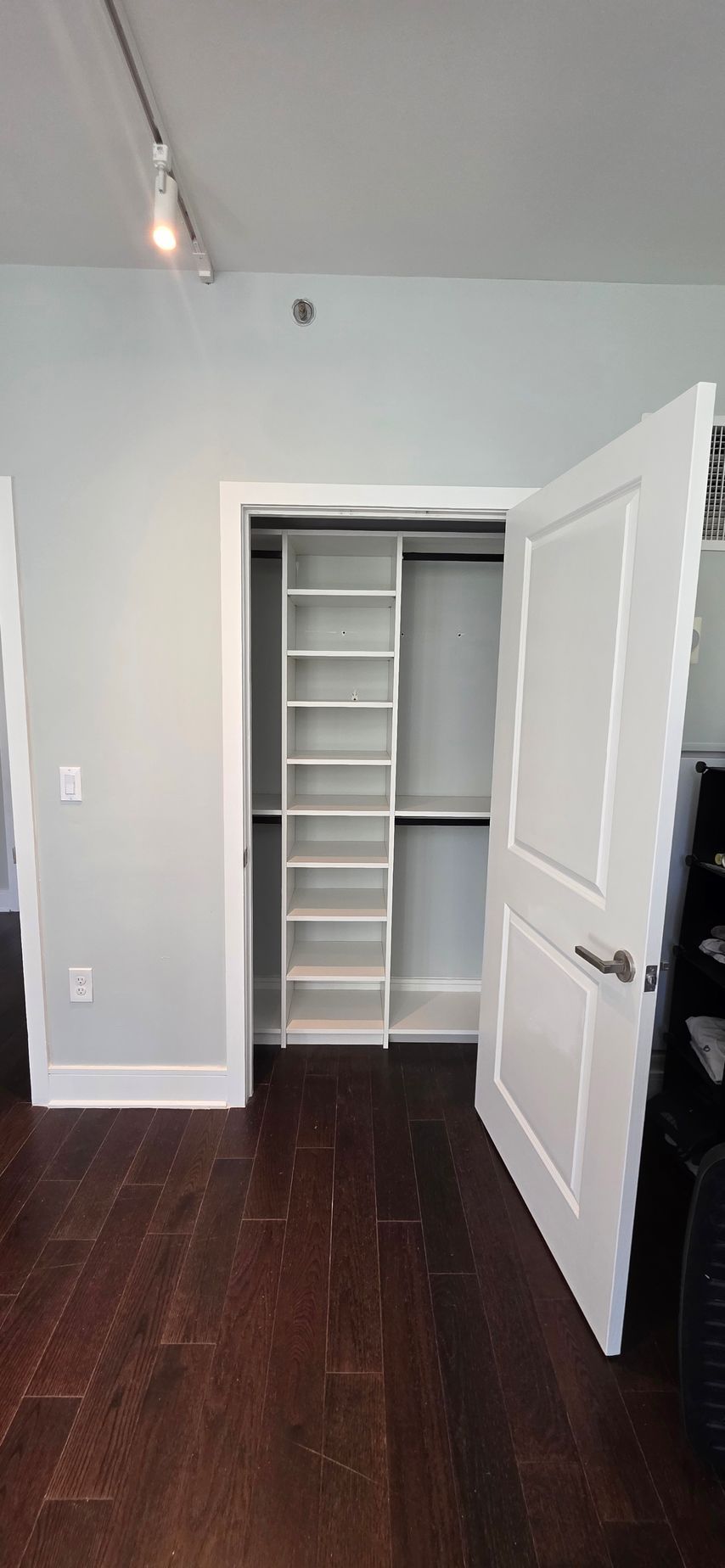 Walk-in closet with white doors and built-in shelves; dark wood floor, light gray walls.