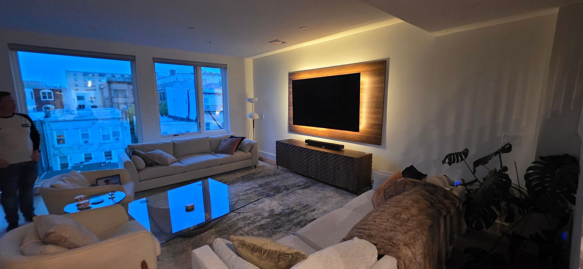 Living room with large TV, couch, and windows with a city view.