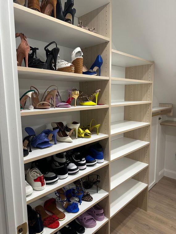 Closet with multiple shelves holding various shoes. Light wood shelves and white walls.