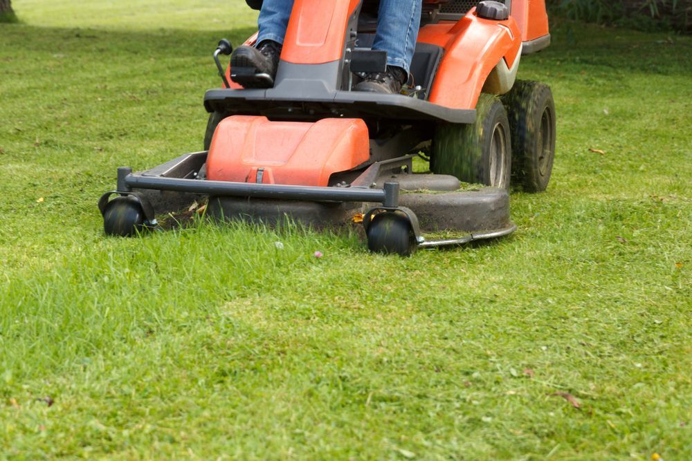 Person On Orange Riding Lawnmower Cutting Green Grass In A Grassy Field — Northern Rivers Acreage Mowing in Byron Bay, NSW