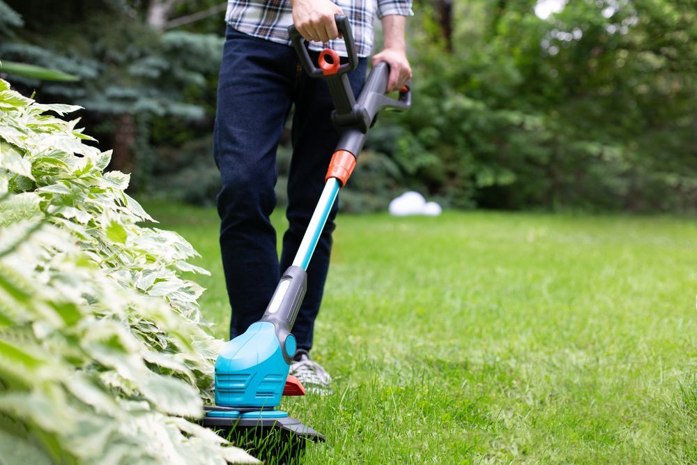 A Person Using A Teal And Black String Trimmer To Edge Grass In A Yard — Northern Rivers Acreage Mowing in Pimlico, NSW