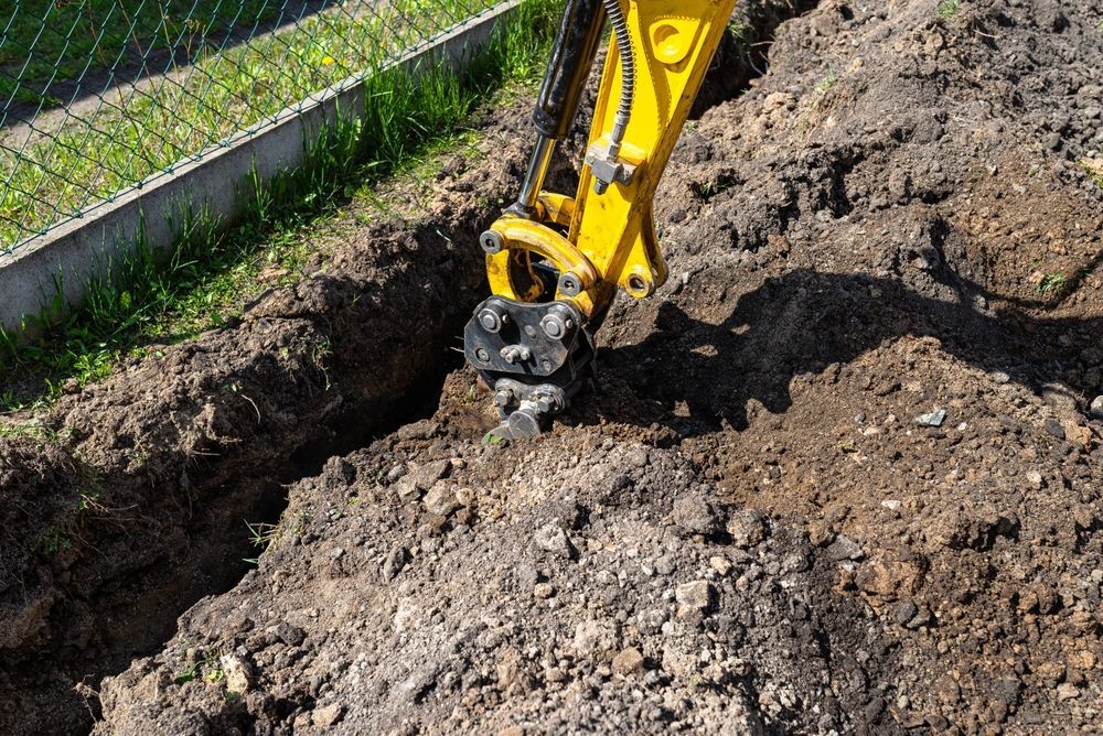 Yellow Excavator Digging A Trench In The Dirt Next To A Fence — Northern Rivers Acreage Mowing in Mullumbimby, NSW