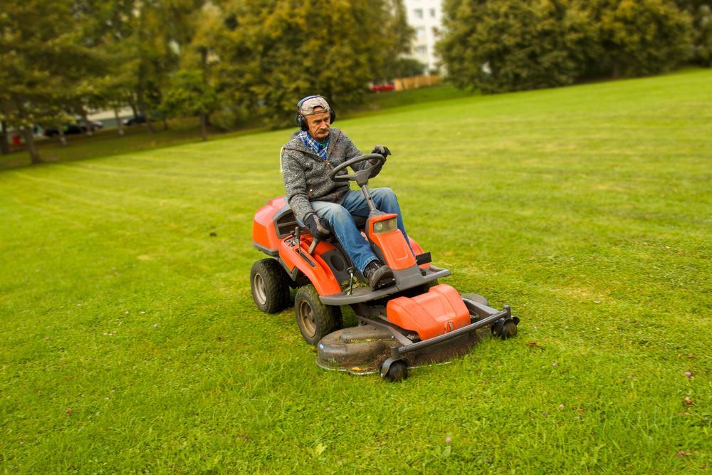 Man Driving An Orange Riding Lawnmower — Northern Rivers Acreage Mowing in Pimlico, NSW