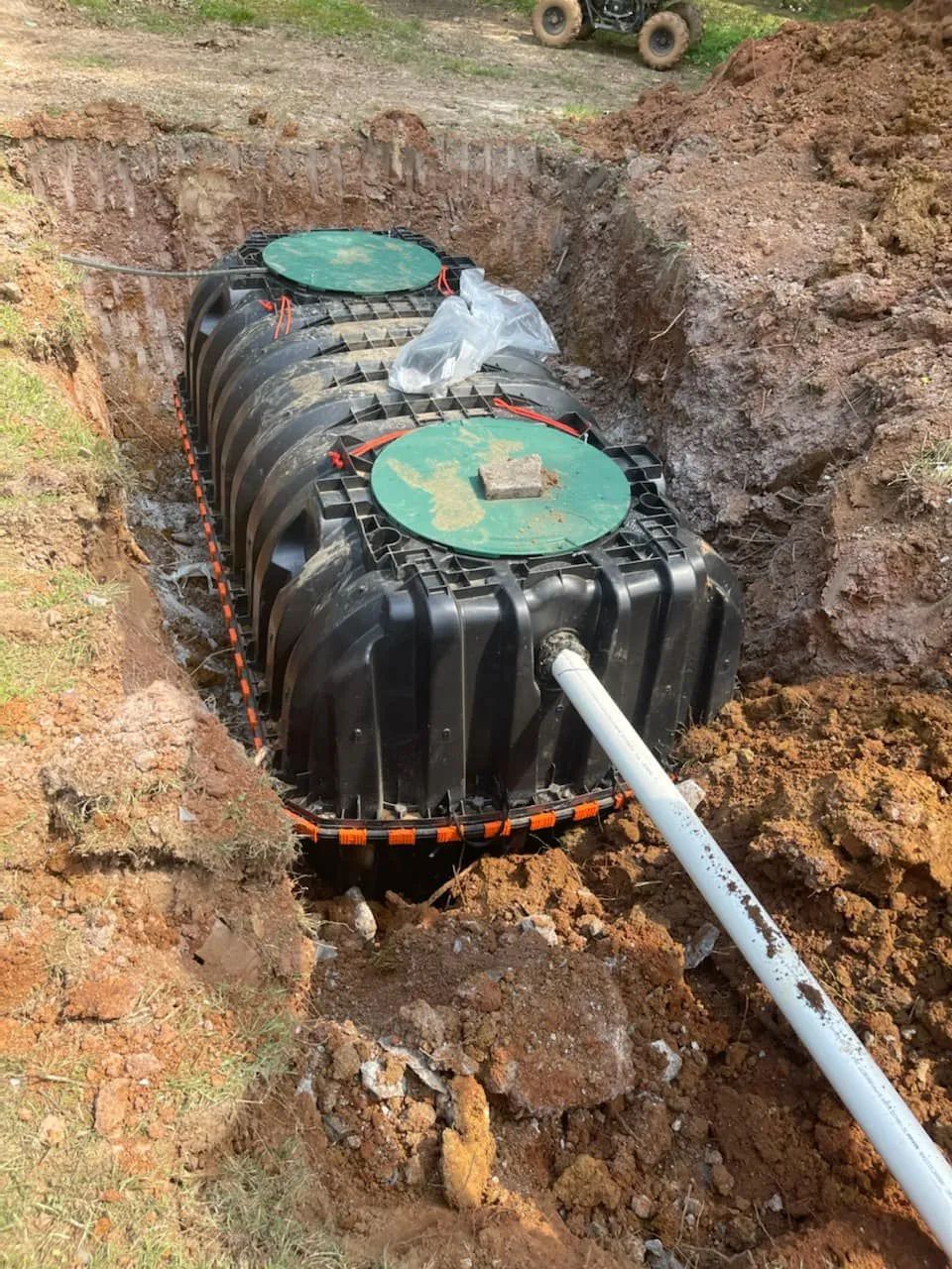 Black septic tank installed in a trench with white pipe and soil around it