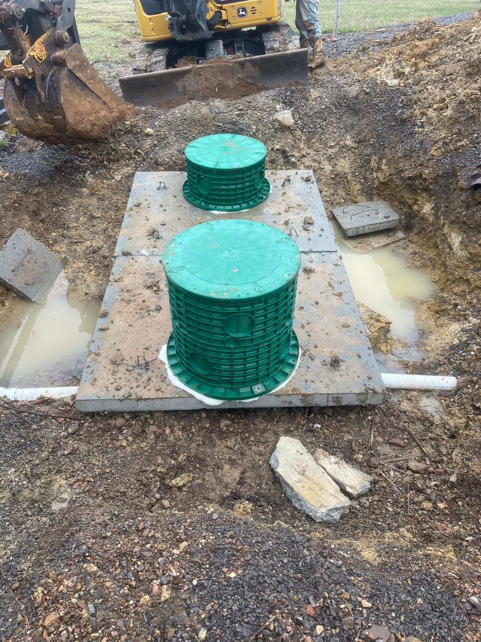 Excavated septic system with two green access covers and a backhoe in the background.