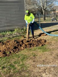 Person in lime green shirt using a tool to work on a post in a grassy yard.