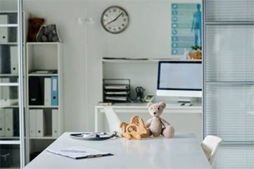 Bright office with white desk, laptop, plush toys, shelves, and wall clock