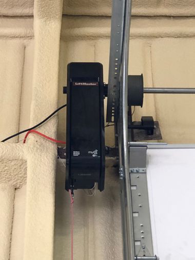 Black garage door opener motor mounted to ceiling beside a metal rail and red pull cord.