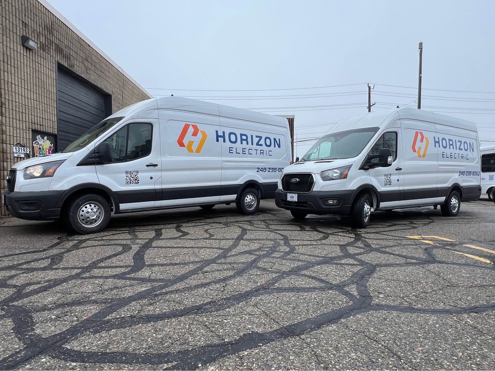 Two white Horizon Electric cargo vans parked side-by-side on an asphalt lot in front of a building.