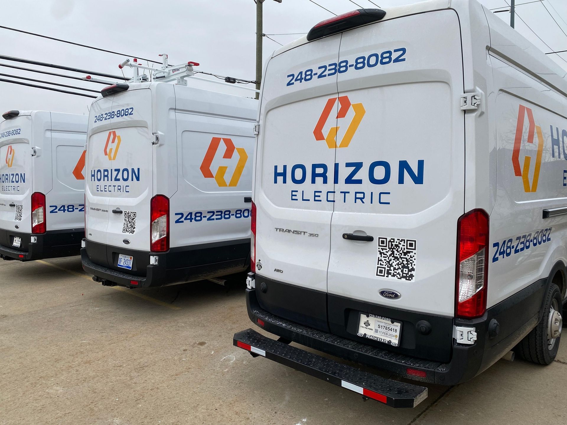 Three white Horizon Electric company vans parked in a row on an asphalt lot.