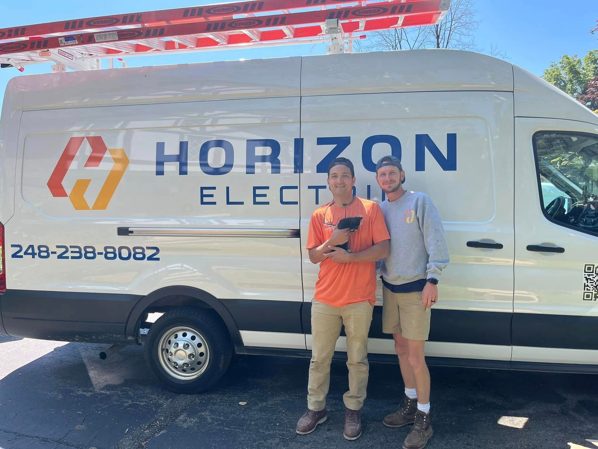 Two people stand smiling in front of a white Horizon Electric work van with the phone number 248-238-8082 on the side.