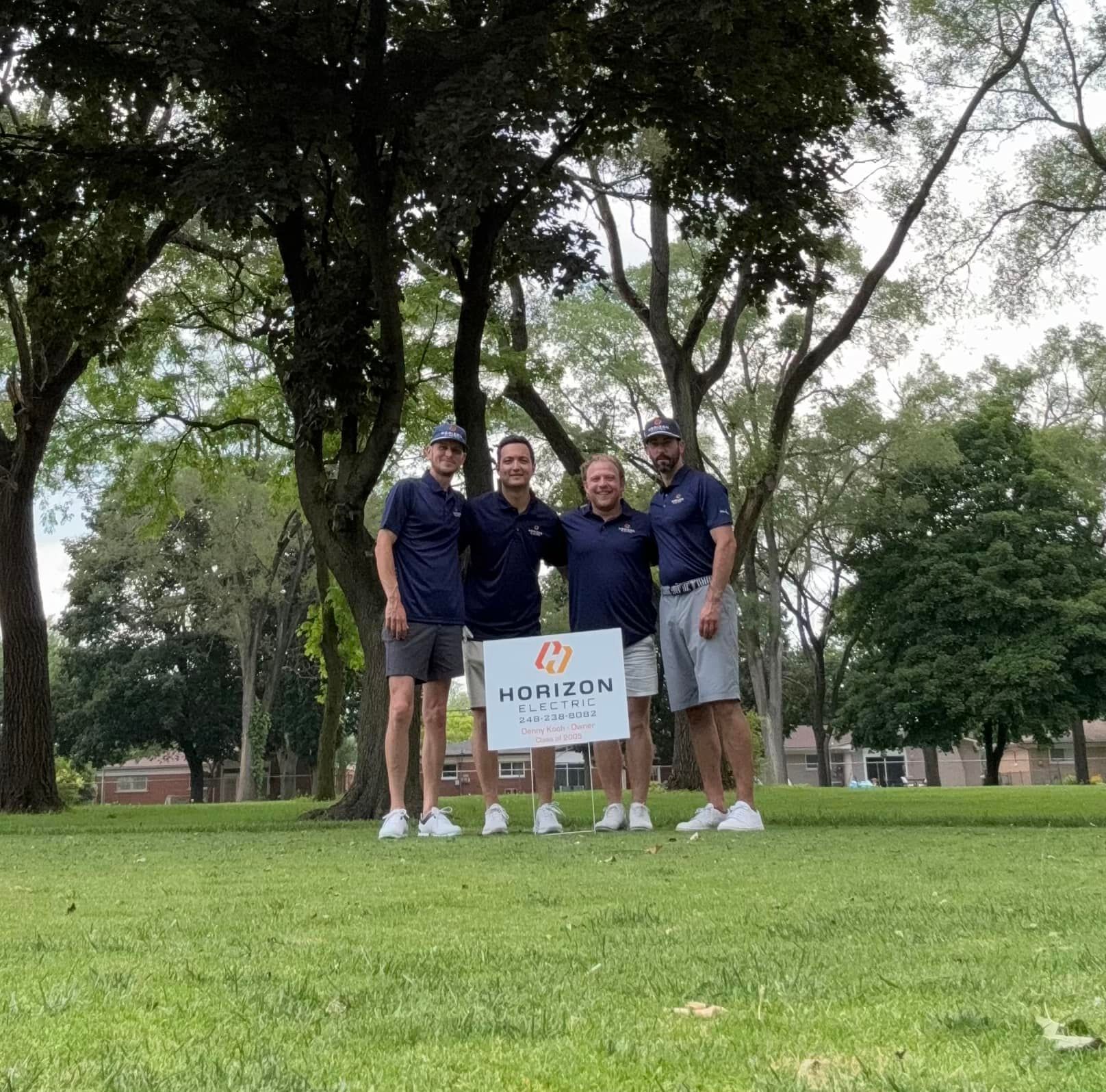 Four men in matching navy polo shirts stand together on a grassy golf course holding a Horizon Wealth Management sign.