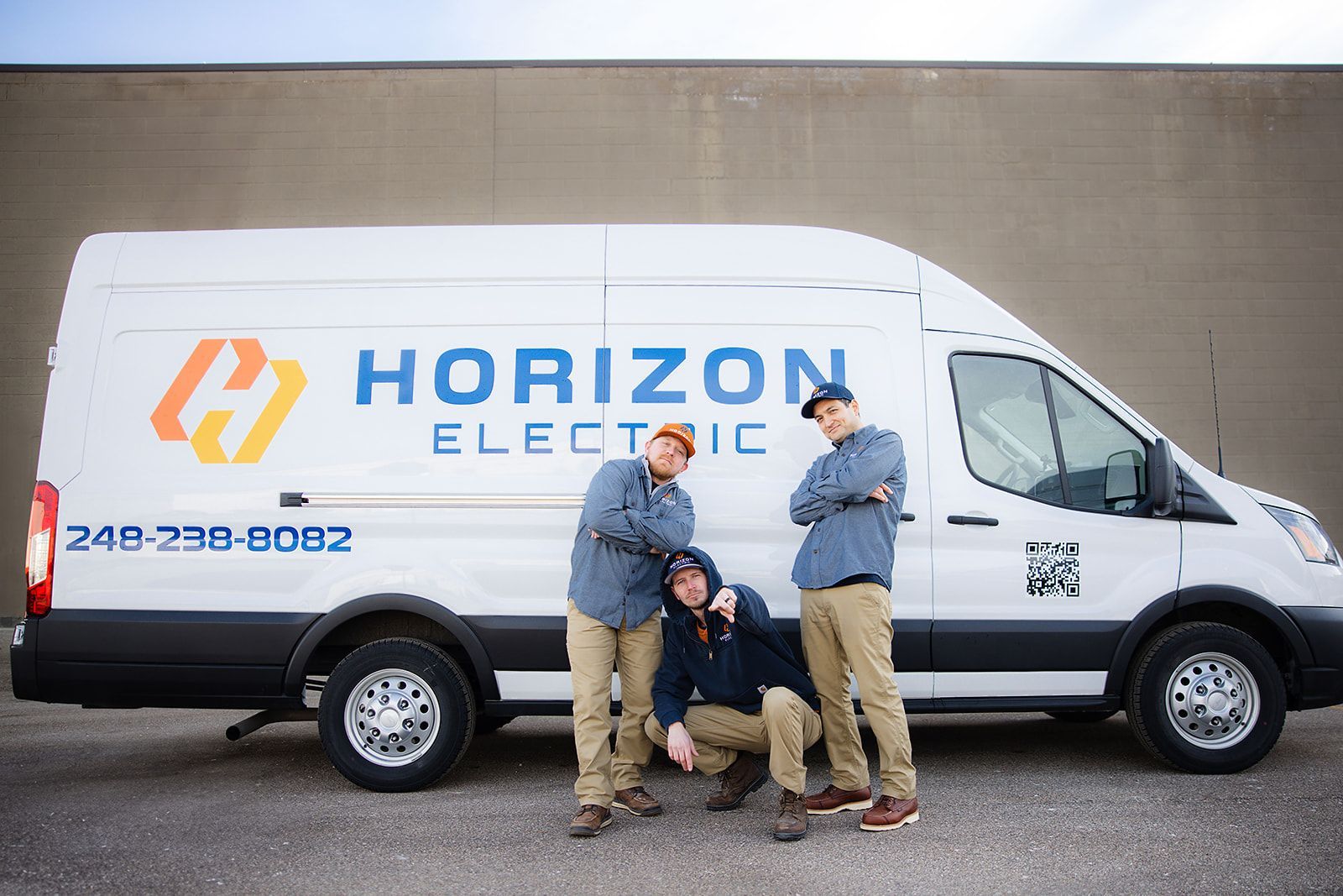 Three workers in work uniforms pose in front of a white Horizon Electric service van parked against a plain wall.