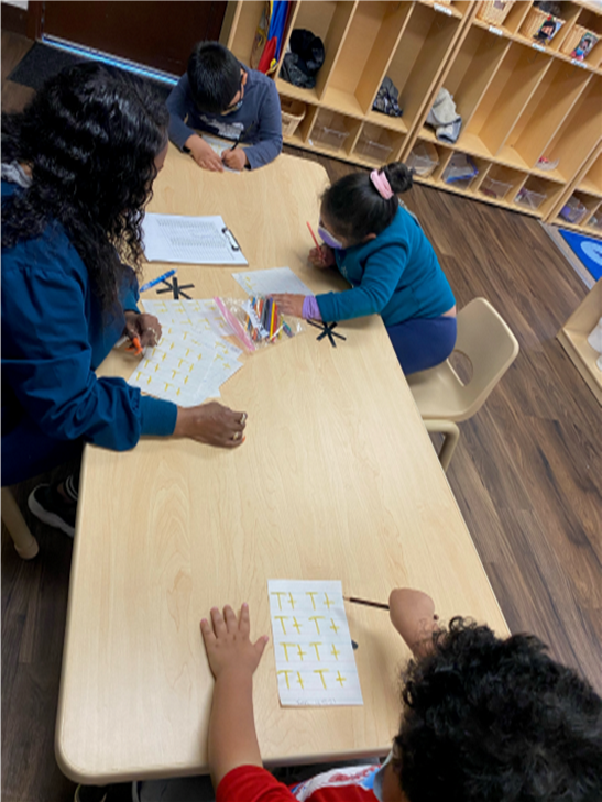 A group of children are sitting at a table with a teacher
