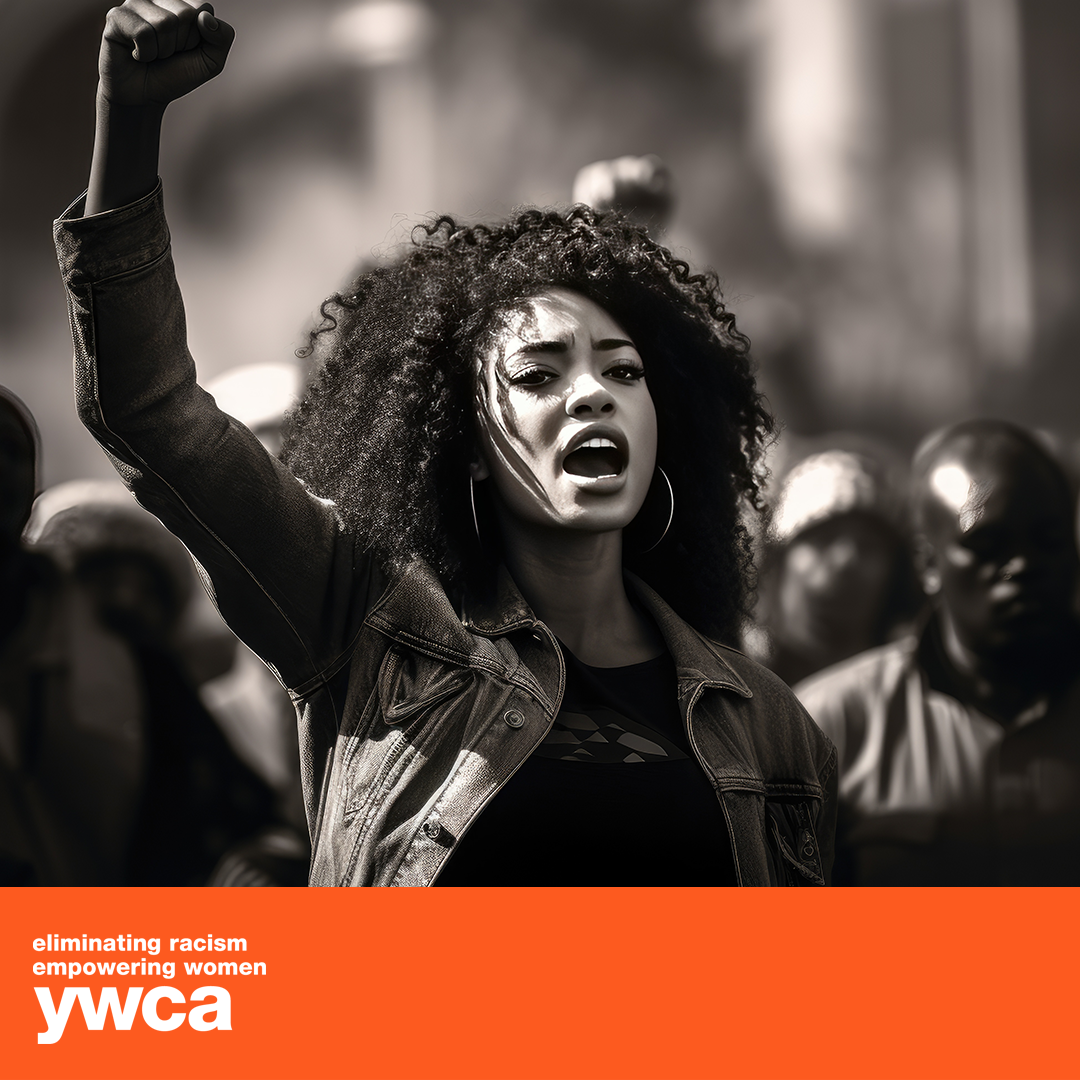 A Black woman raises her fist in protest, yelling with a crowd in the background