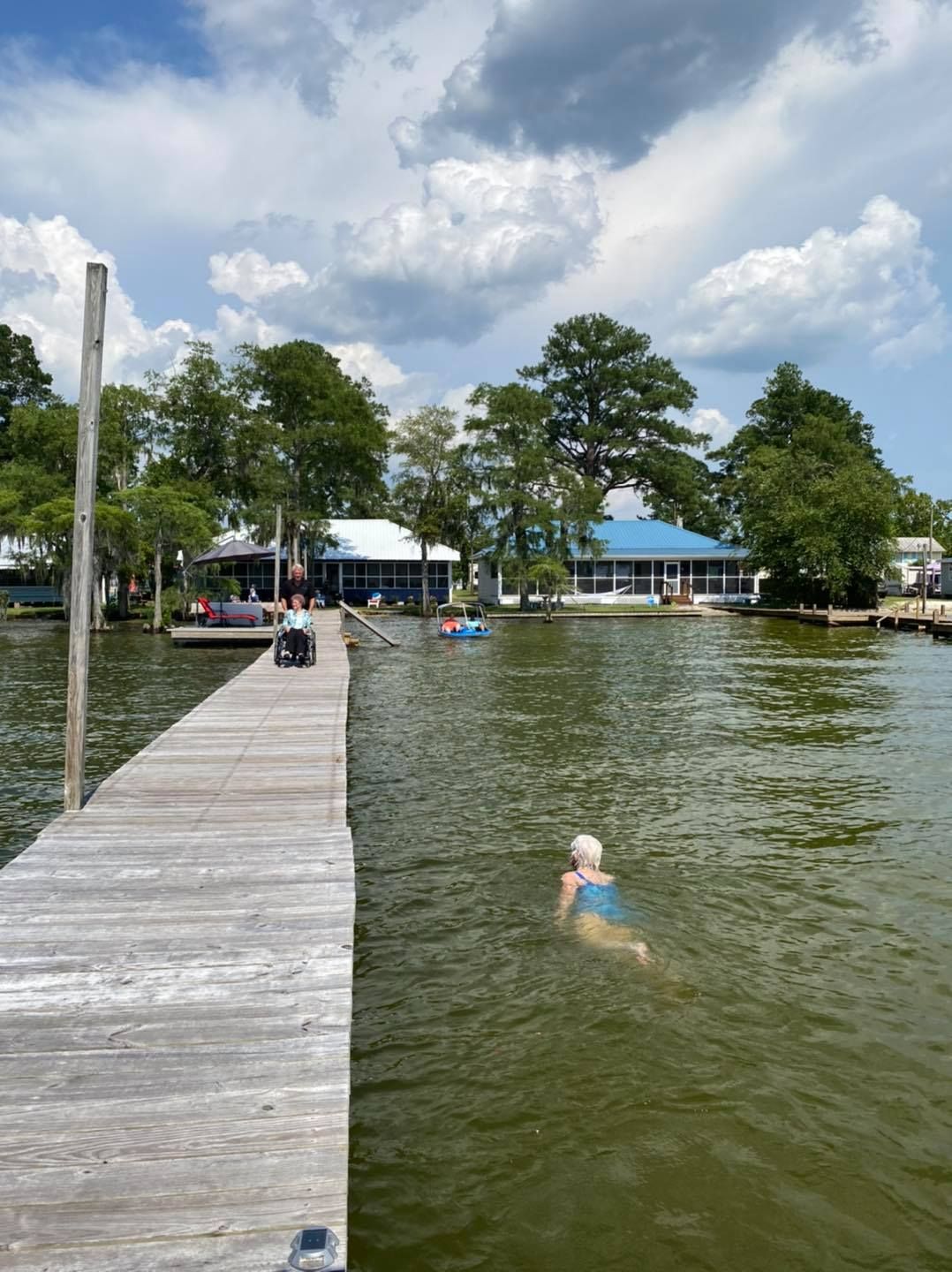 A person is swimming in a lake near a dock
