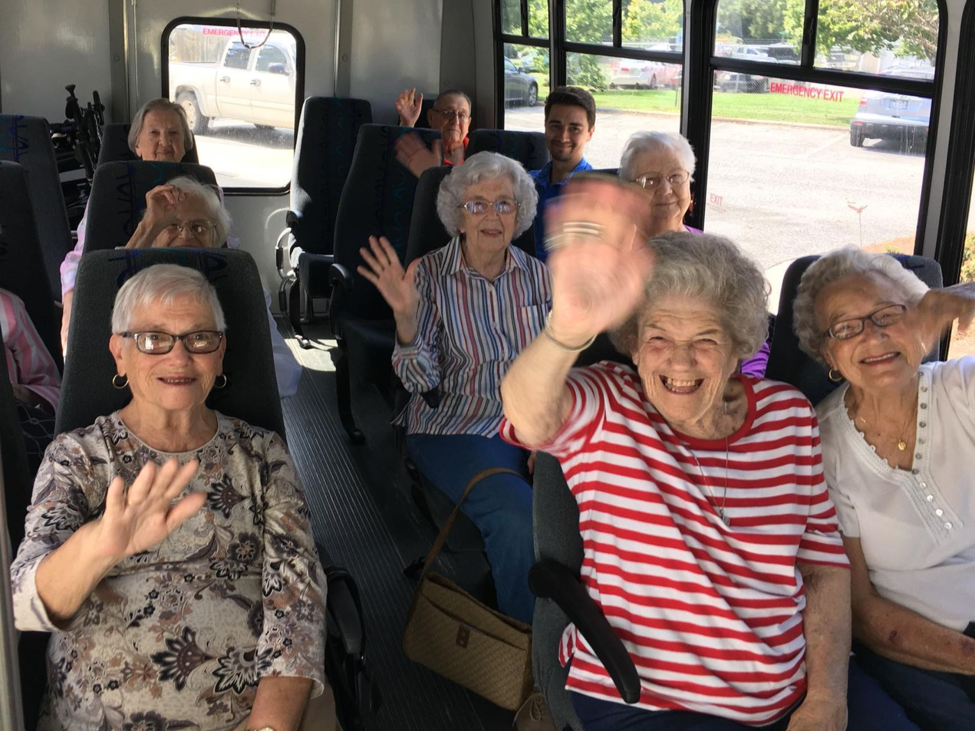 Group of people waving from inside a bus. Independent senior living community near Jacksonville, NC.