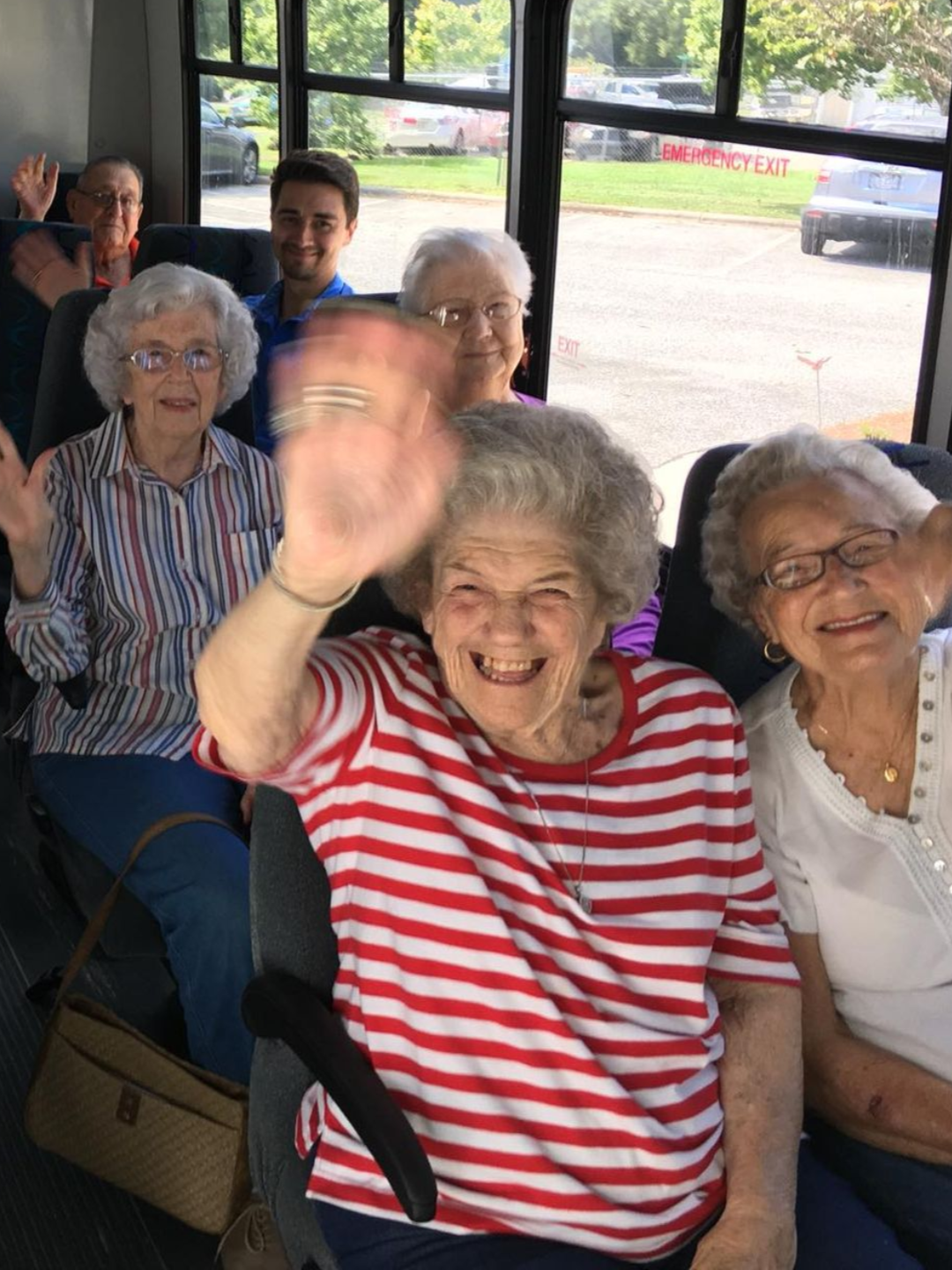 Group of people waving from inside a bus. Independent senior living community near Raleigh, NC.