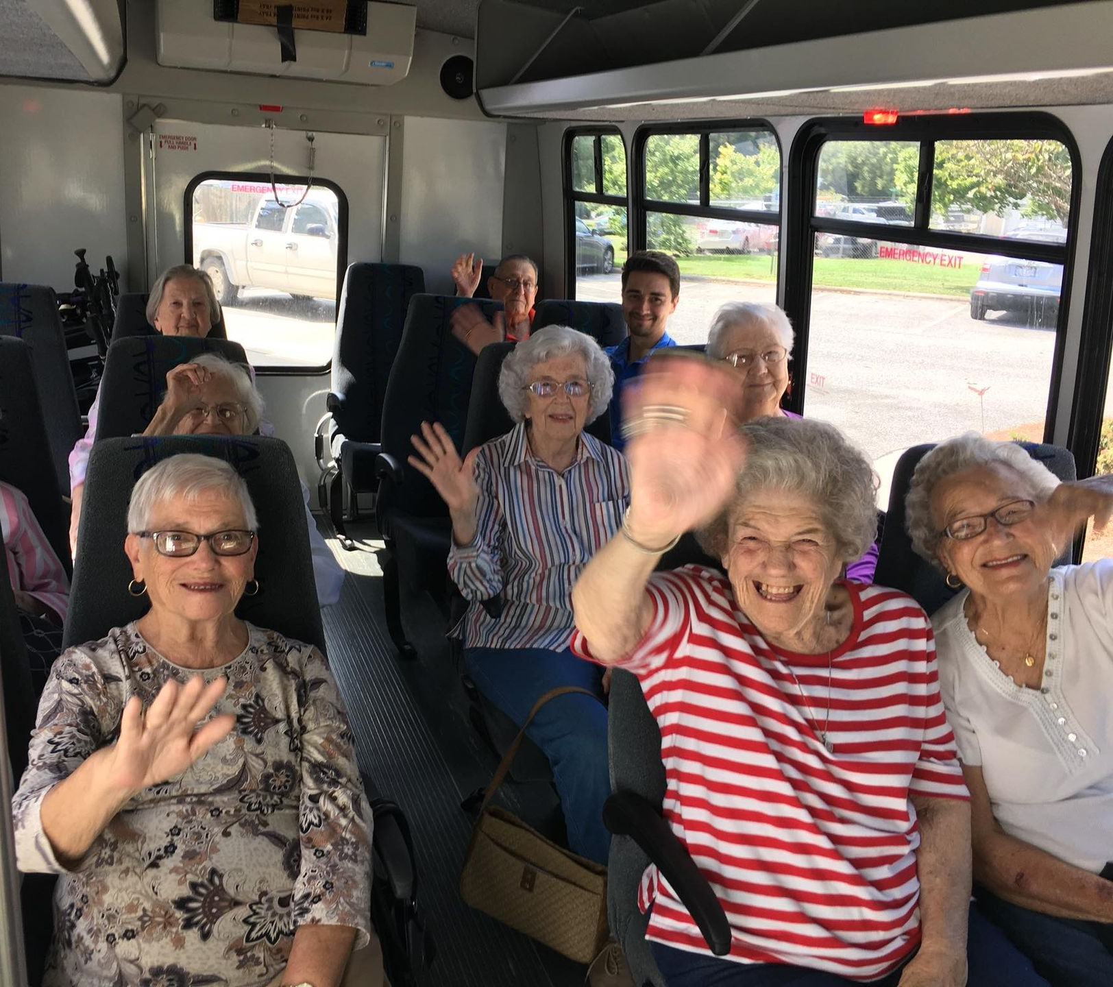 People waving from inside a bus. Passengers are seated, smiling, near windows. Senior retirement community near Goldsboro NC.