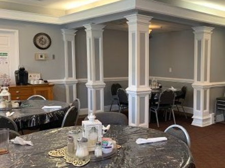 Dining room with round tables, black chairs, gray walls, and white columns. Independent senior living community near Jacksonville, NC.