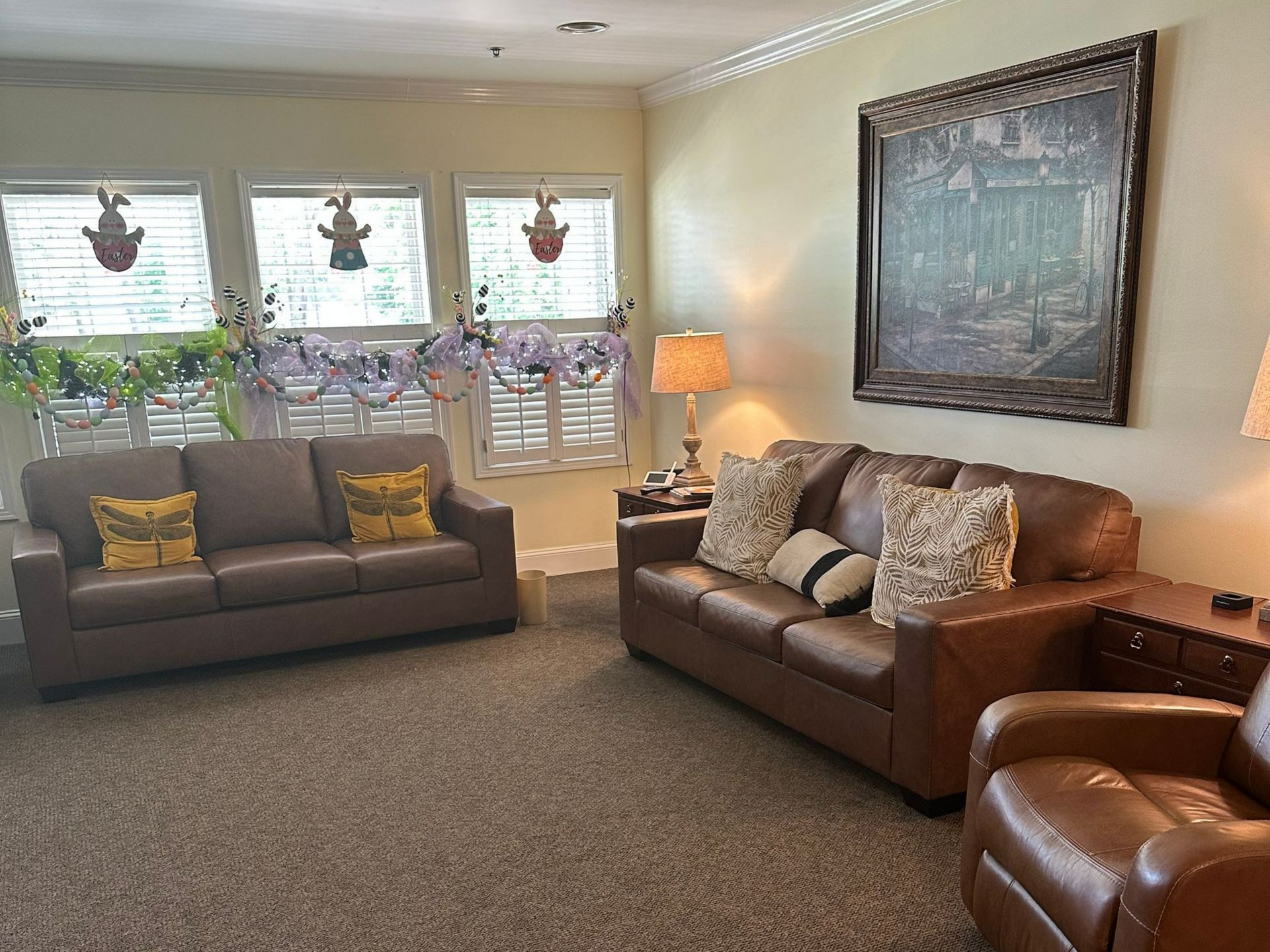 Cozy living room with two sofas, brown recliner, framed wall art, lamp, and window plants near Smithfield, NC.