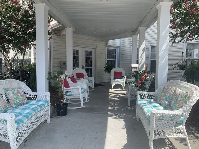 A porch with wicker furniture and rocking chairs under a canopy.