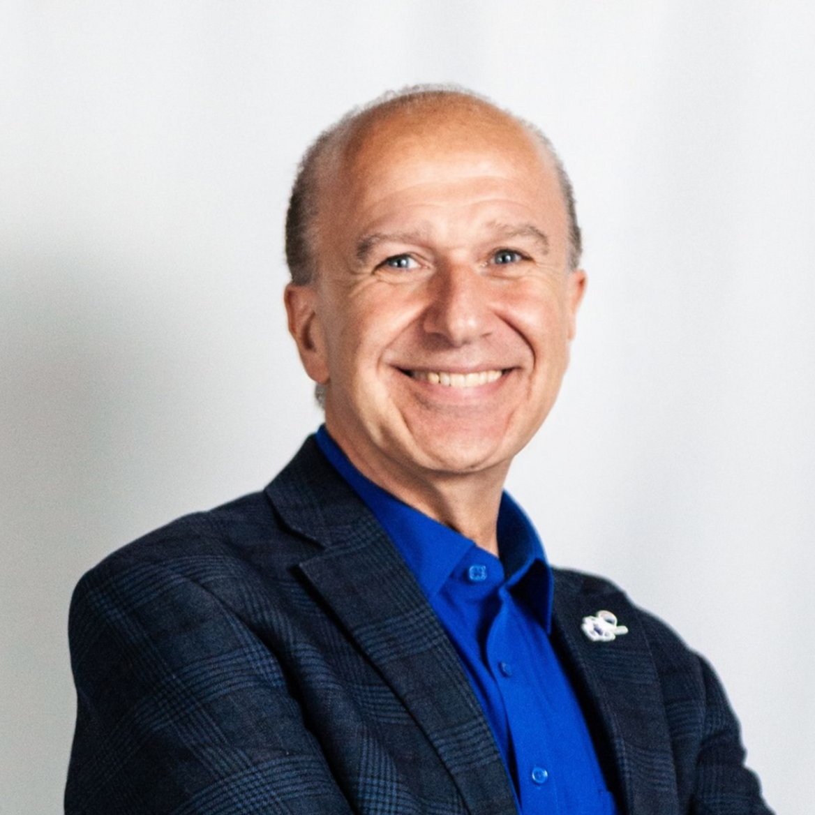 Smiling man in a blue shirt and dark blazer against a light background