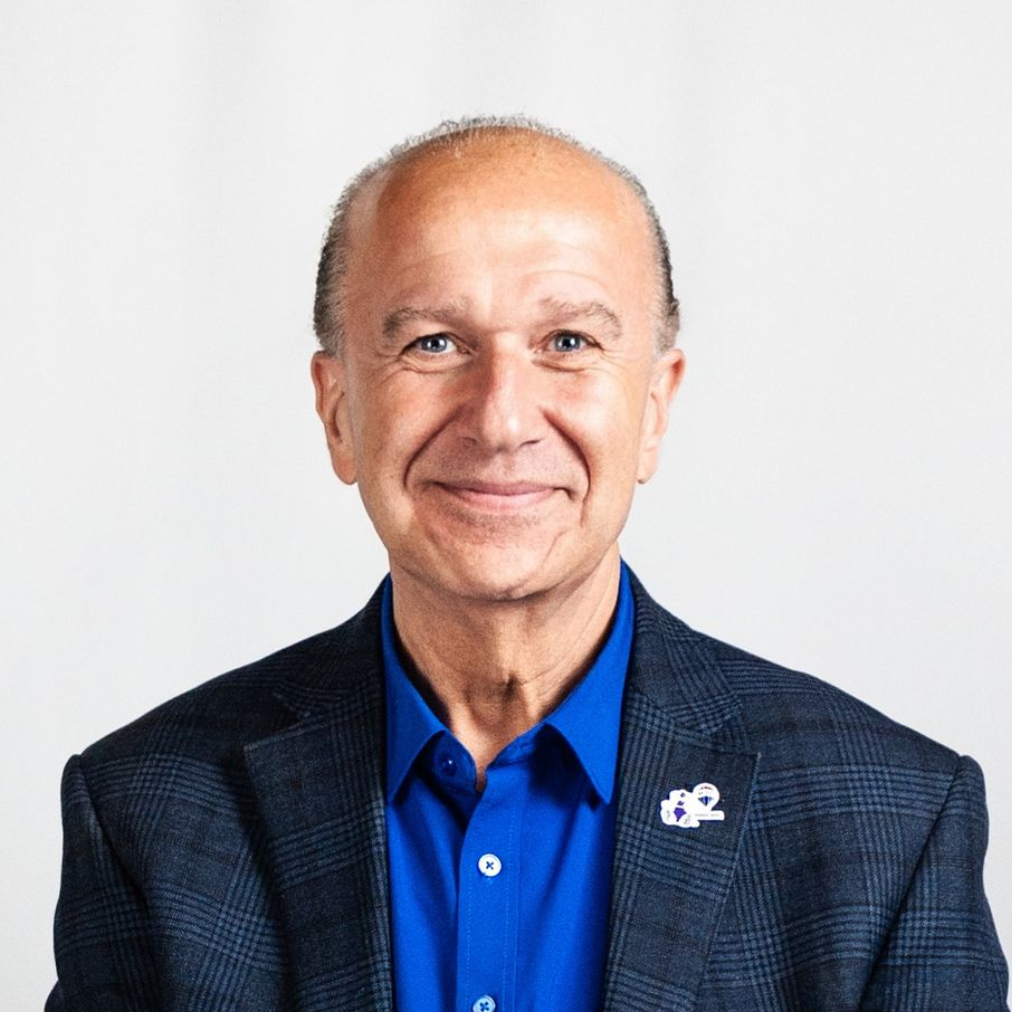 Smiling person in a blue shirt and dark blazer against a white background