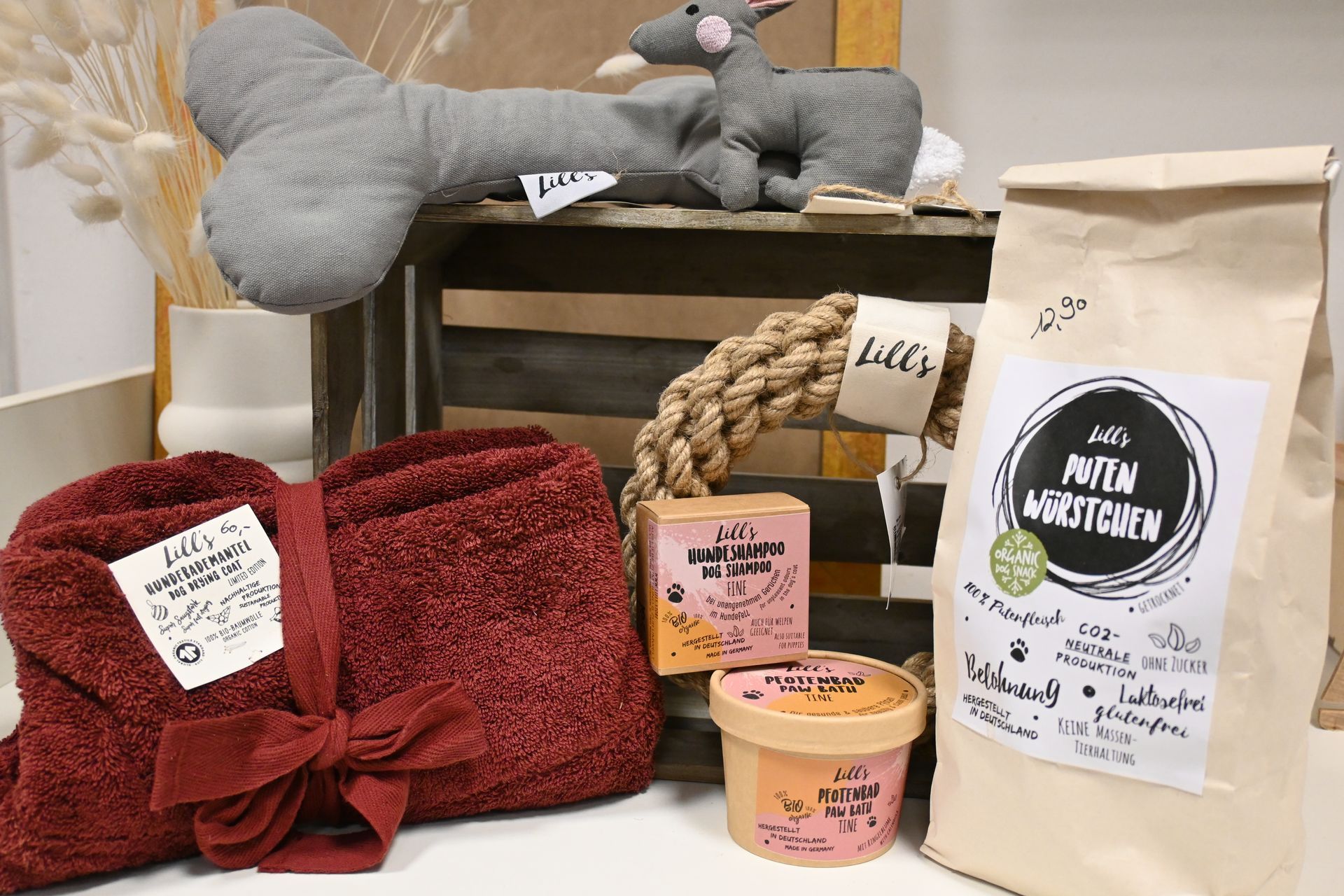Ein Geschenkkorb mit Handtüchern, Kerzen, Snacks und einer beigefarbenen Geschenktüte steht auf einem Regal.