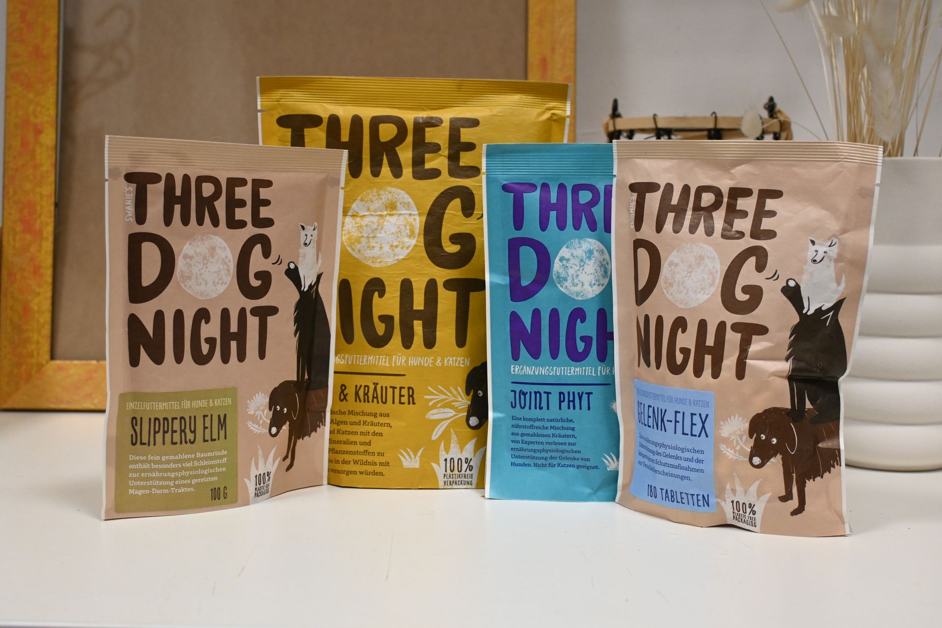Vier Exemplare des Buches „Three Dog Night“ mit beigen, goldenen, blauen und weißen Einbänden stehen in einem Regal.