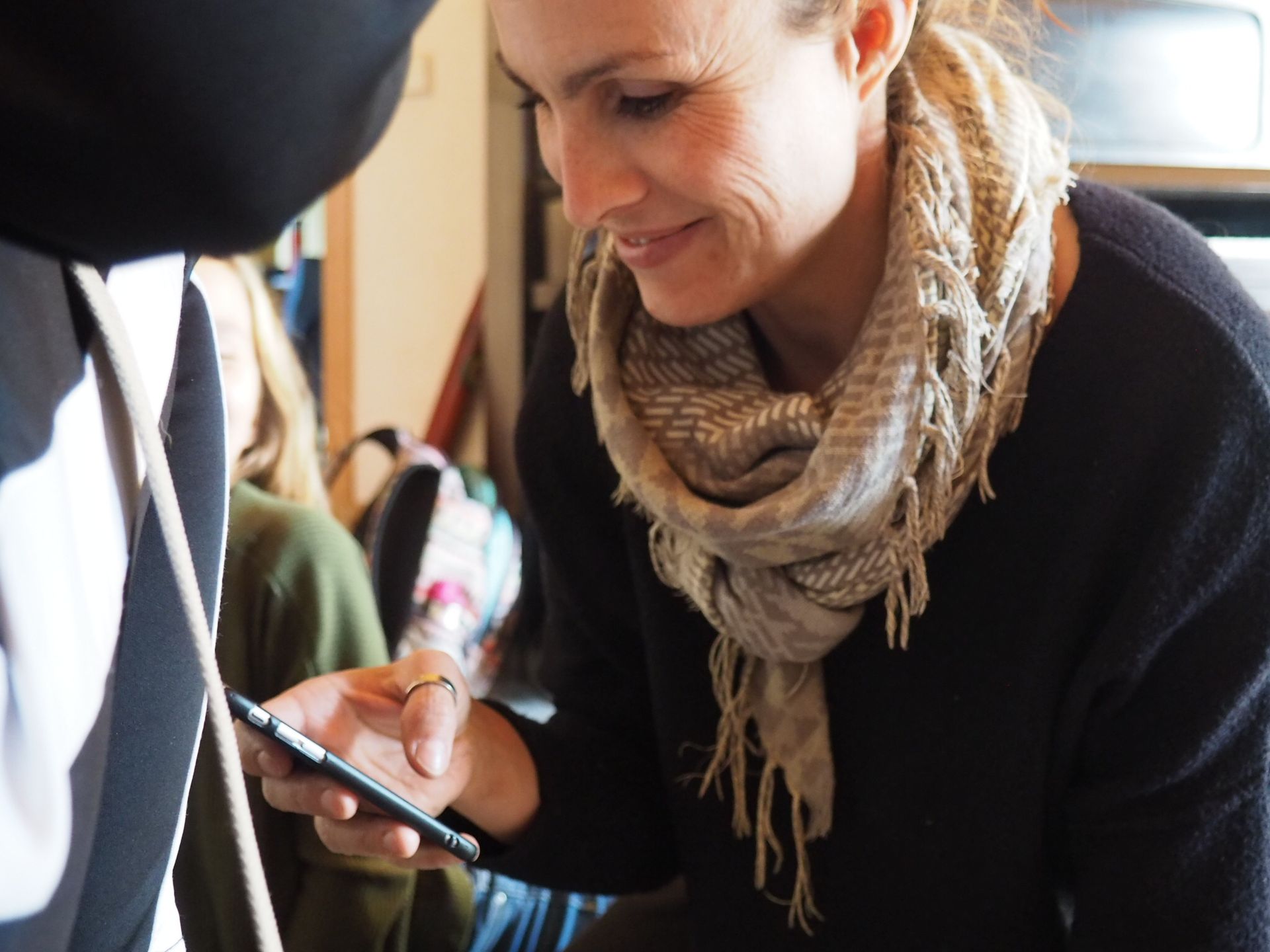 Eine lächelnde Frau benutzt ihr Smartphone, während sie drinnen steht. Sie trägt 