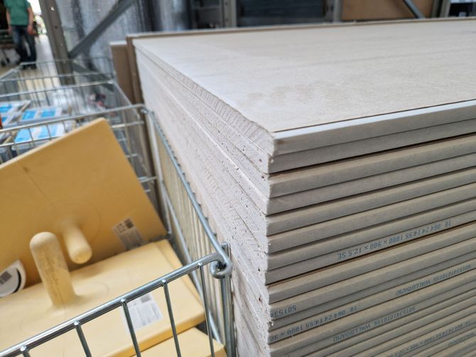 Stack of drywall sheets on a warehouse cart, with a yellow box and metal railing nearby.