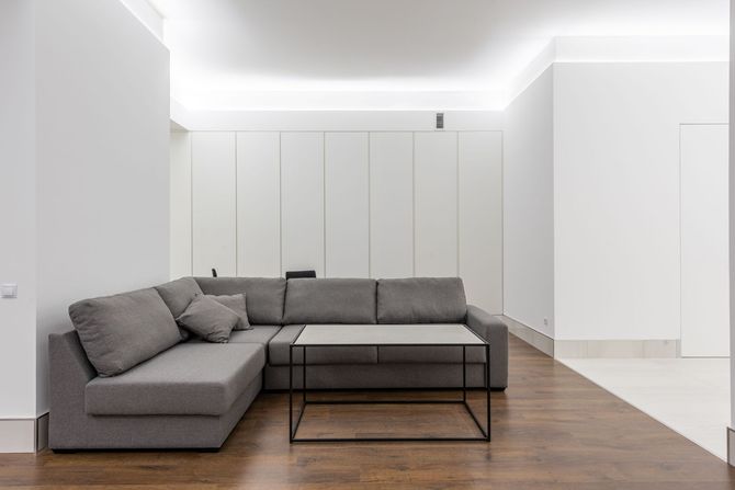 Gloved hand sanding or scraping the corner of a white wall indoors