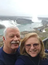 Two smiling people pose before a misty waterfall viewpoint.