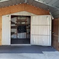 Open shed with white sliding doors, corrugated metal walls, and a hanging black bag inside.