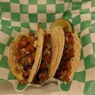 Two tacos on green checkered paper with a lime wedge in the background