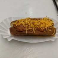 Hot dog topped with chili and shredded cheese in a paper tray on a white table