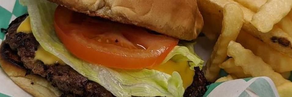Close-up of a burger with tomato, lettuce, and fries on the side