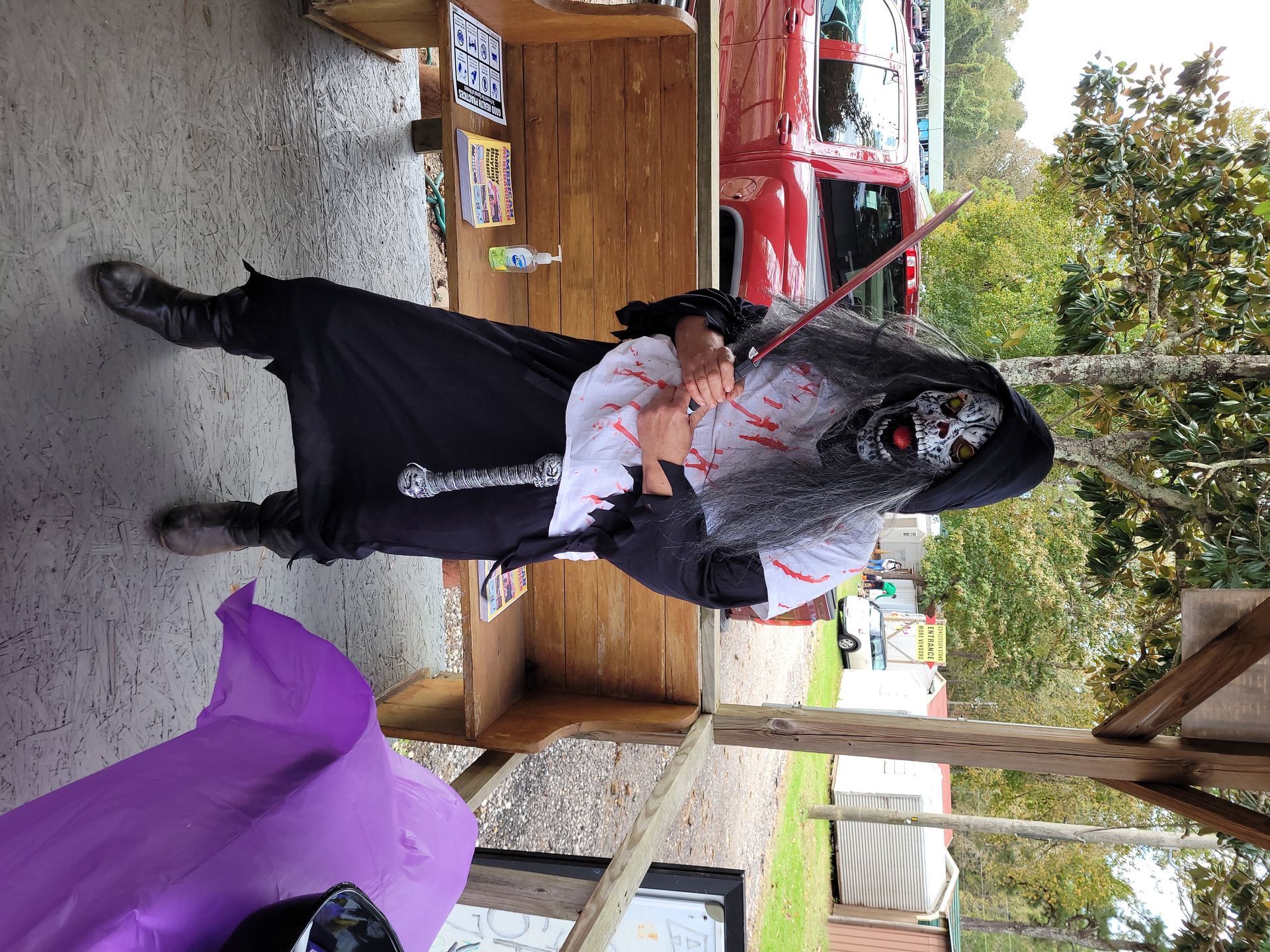 Person in black outfit and white shirt holding a large gray prop in an outdoor patio area.