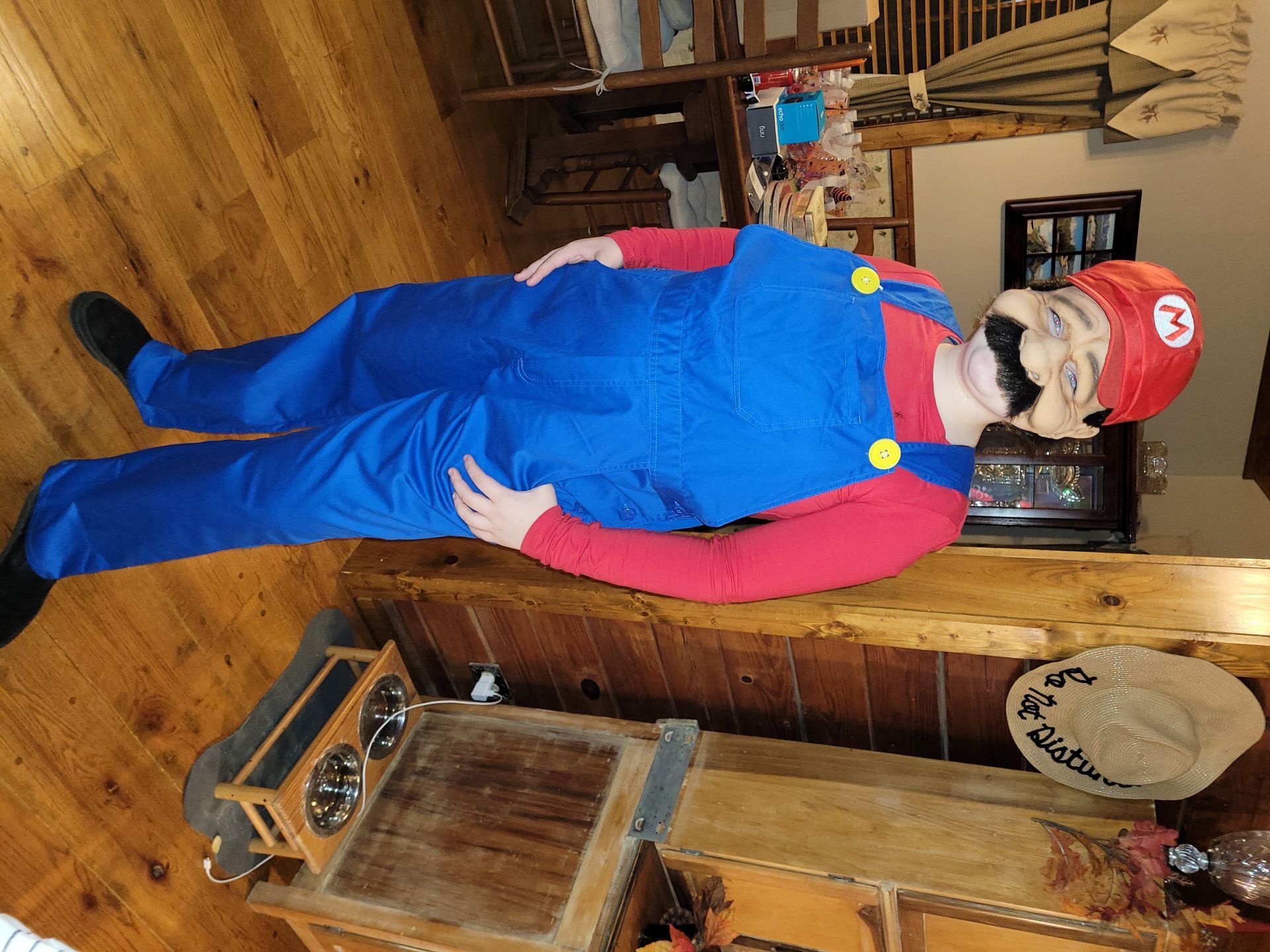 Person in a Mario costume standing in a wooden room beside a wood stove and bench.
