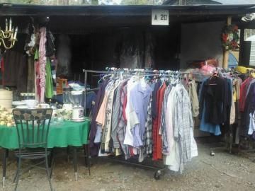 Outdoor market stall with racks of hanging clothes and a green-covered table under a dark awning