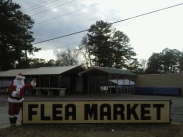 Santa beside a large Flea Market sign outdoors on a cloudy day