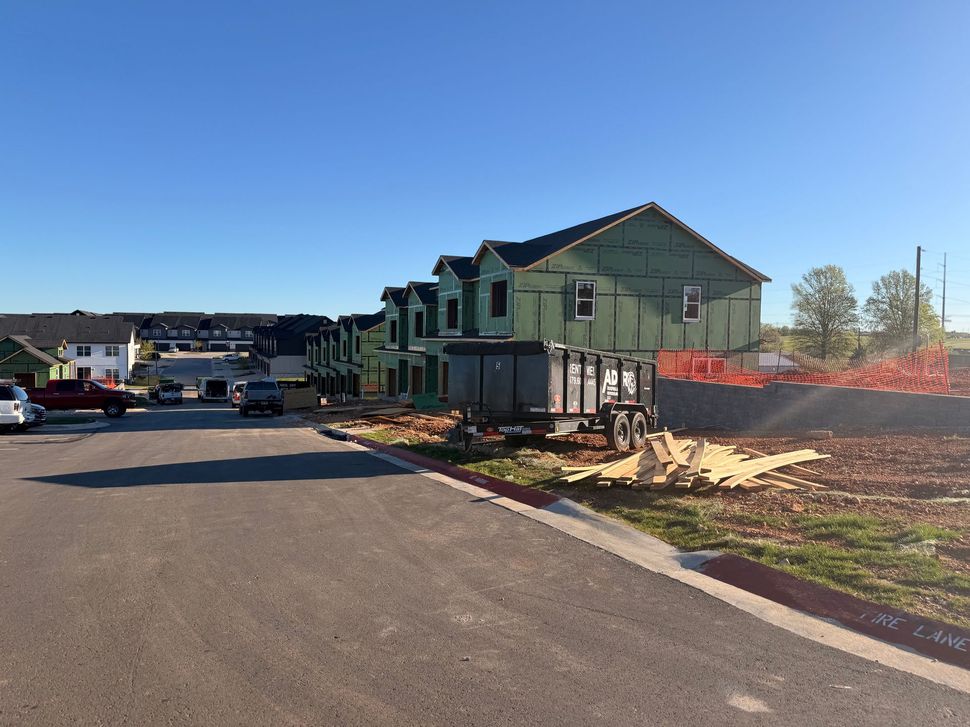 Workers install roofing on new homes with green exterior walls under construction in a suburban development.
