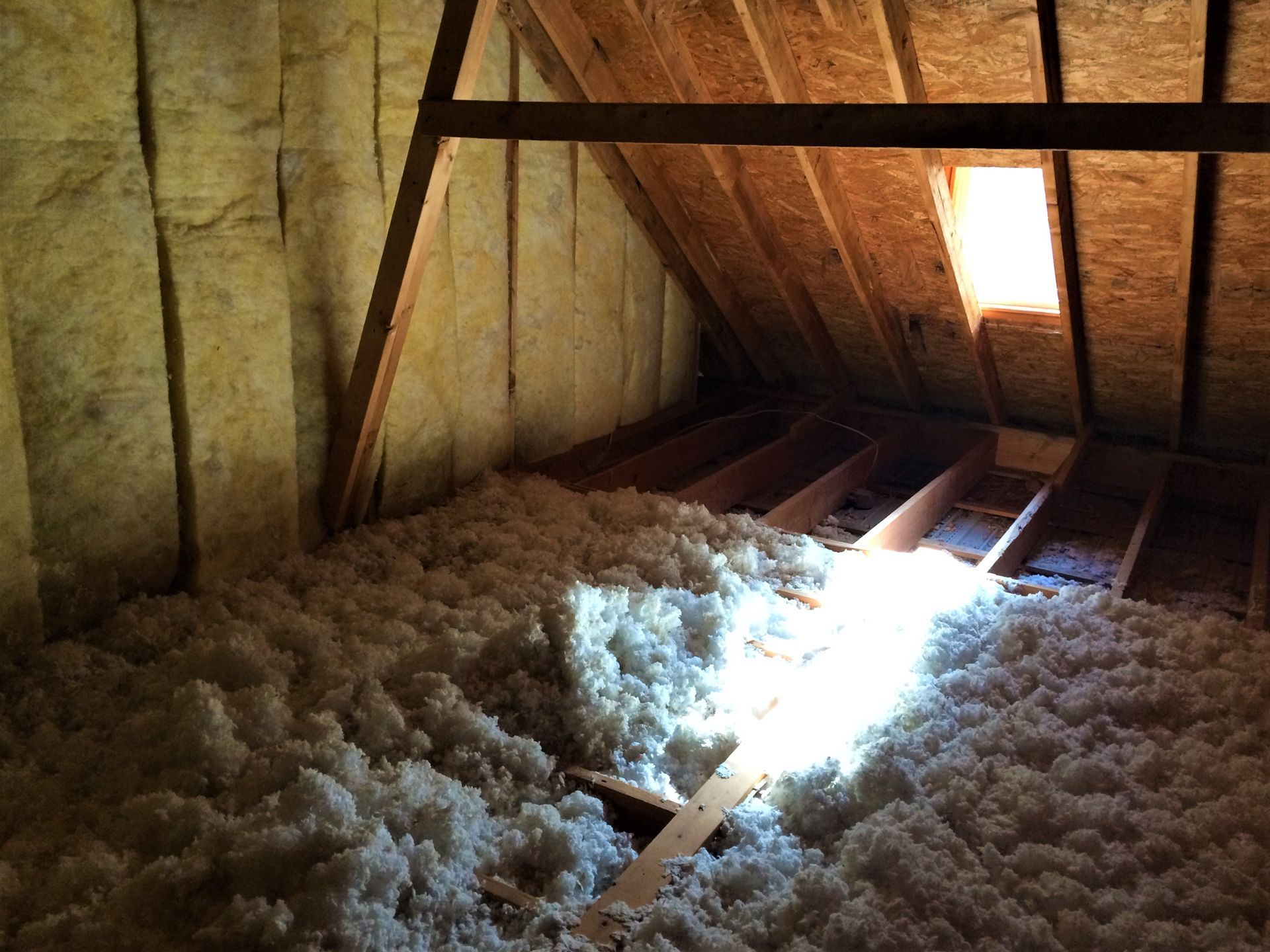 Interior view of an attic with insulation, a skylight, and wooden beams