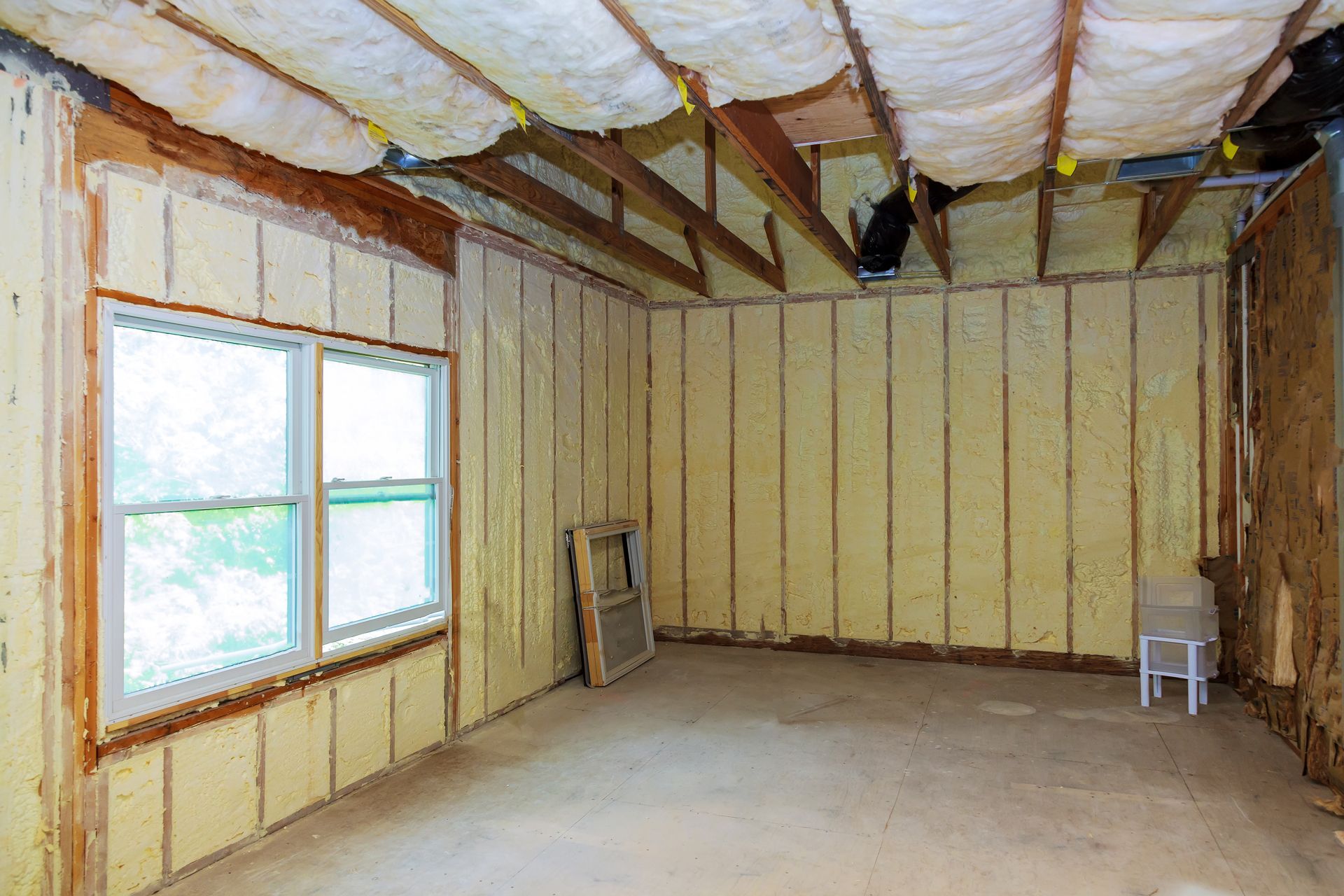 Interior view of a room with spray foam insulation on walls and ceiling, a window, and a small white chair